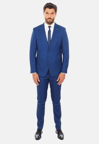 Completo su misura blu con giacca a due bottoni, revers sciallati e pantaloni abbinati. Camicia bianca, cravatta blu e scarpe in vernice nera.