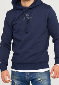 Mörkblå hoodie gjord av mjukt tyg, med dragsko i huvan, ribbade ärmslut och en diskret logotyp tryckt på bröstet.