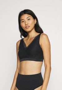 Black wireless bralette featuring a V-neckline with lace trim, smooth fabric, and a wide underband for support. Paired with high-waisted black briefs.