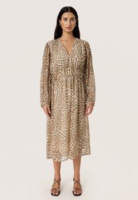 Løveprint midi-kjole med V-udskæring, draperet talje og lange ærmer. Lavet af let, gennemsigtig stof. Kombineret med sorte sandaler med stropper.