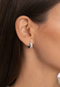 Pendientes geométricos de plata con un diseño hexagonal, que presentan una superficie suave y pulida y un cierre negro seguro.