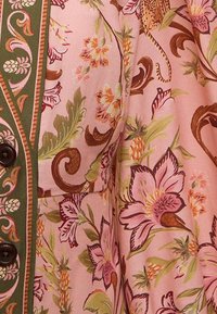 Tissu à motifs floraux en rose, avec des accents verts et un detailing complexe. Le matériau a une texture lisse avec des boutons à l'avant.