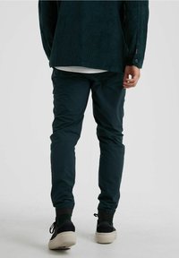 Mörkgrön corduroyskjorta med avslappnad passform, matchad med smalt skurna, mörkgröna stretchbyxor och svarta sneakers.