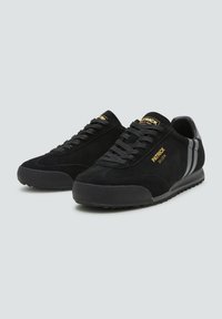 Sneaker in suede nera con punta tonda, dotate di branding dorato, lacci neri e strisce laterali grigie. Suola in gomma testurizzata per una migliore aderenza.