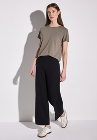Khaki tričko s krátkým rukávem, černé volné kalhoty a béžové tenisky s bílými šněrovadly; minimalistický design a hladká textura látky.