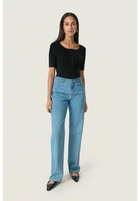 Top negro acanalado de manga corta con detalle de botones, combinado con jeans de pierna ancha azul claro, y calzado negro de punta.