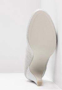 Semelle de chaussure à talons hauts en suède gris avec un accent argent scintillant, présentant une surface en caoutchouc texturé et un design à bout pointu.