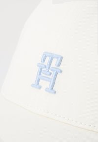 Cappello bianco con un logo ricamato in rilievo di colore azzurro chiaro, caratterizzato da una trama di tessuto liscia e un design strutturato. Presente un delicato dettaglio di cucitura.