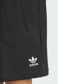 Shorts neri Adidas con tessuto testurizzato, dotati di tasche laterali e un logo bianco con tre righe vicino all'orlo.