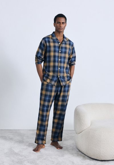 Pyjamasset med rutig mönster i blått och gult, med en skjorta med knappar och matchande byxor med avslappnad passform. Tillverkad av mjukt tyg.