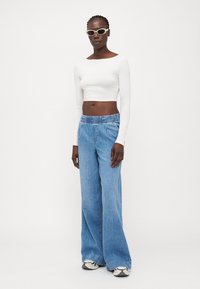 Beli dolg rokav crop top v kombinaciji z svetlo modrimi širokimi hlačami z elastičnim pasom. Sivo-bele superge dopolnjujejo videz.
