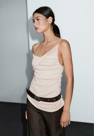 Top aderente di un rosa chiaro con spalline sottili e design attorcigliato; abbinato a pantaloni marrone scuro e una cintura nera con hardware in argento.