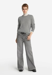Szary sweter dziany z okrągłym dekoltem, w zestawie z luźnymi, wysokim stanem szarymi dżinsami. Czarni pasek i błyszczące czarne buty dopełniają strój.
