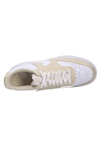 Zapatillas Nike con parte superior de cuero beige y detalles en blanco, caja de puntera perforada y cordones blancos. Suela de goma plana y forma redondeada.