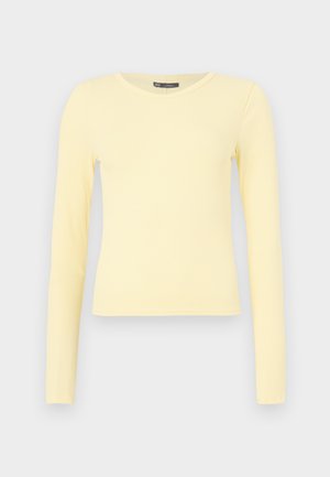 Chemise à manches longues jaune clair côtelée avec un col rond et un ourlet légèrement raccourci sur un fond uni.