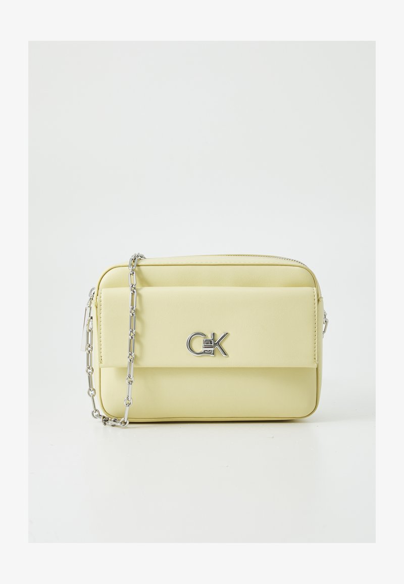 Sac en cuir synthétique jaune en bandoulière avec une chaîne argentée, comportant une poche avant et un détail de logo métallique proéminent.