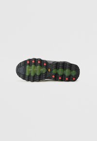 La semelle extérieure de la chaussure de sport noire présente une semelle en caoutchouc épaisse et texturée avec des accents verts et rouges, offrant une bonne adhérence et une durabilité.