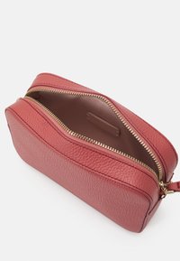 Czerwona torebka skórzana z wypukłą strukturą, z złotym zamkiem błyskawicznym, o owalnym kształcie i gładkim wnętrzu. Zamek biegnie wzdłuż górnej krawędzi, odsłaniając przestronną komorę.