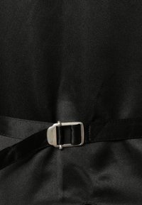 Tissu noir avec une boucle rectangulaire argentée qui attache une sangle noire autour de la taille.