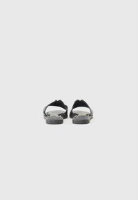 Sandales noires avec une semelle plate, bout ouvert et design à T. Fabriquées en matériau lisse, elles présentent un minimum de détails et une silhouette simple.
