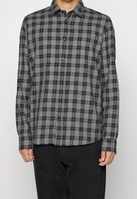 Camisa de botones en patrón de cuadros en negro y gris, hecha de una tela suave, con cuello y mangas largas con puños abotonados.