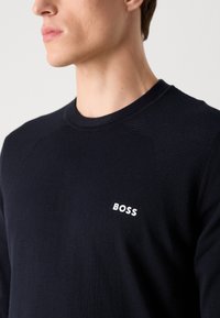 Sötétkék, crew-neck pulóver, texturált anyagból készült. Elülső részén egy fehér "BOSS" logó található, a vállrészen pedig diszkrét bordázott részletek láthatók.