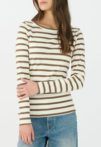 Maglietta a maniche lunghe a righe in crema e marrone. Tessuto morbido e elastico con scollo a barca e design attillato. Abbinata a jeans azzurri chiari.