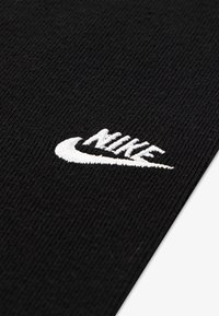 Črna nogavica z rebrasto teksturo in belo vezeno Nike logo. Oblikovanje vključuje klasičen, elastičen kroj za udobje in vzdržljivost.