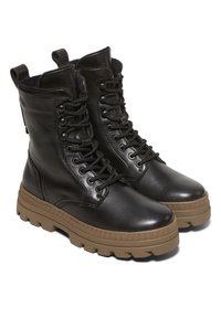 Bottes en cuir noir à lacets avec semelles en caoutchouc beige épaisses et languettes sur fond blanc.