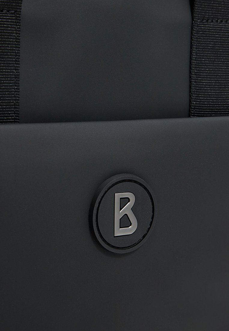 Schwarzer Rucksack mit einem runden Logo, das ein erhabenes "B" in silberner Farbe zeigt, ergänzt durch strapazierfähige schwarze Träger. Glatte Textur.