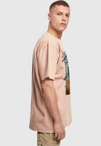 Lyserød bomulds t-shirt med korte ærmer, der har et farverigt grafisk tryk på forsiden. Løs pasform, rund udskæring og blød tekstur.