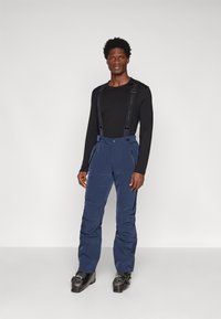 Navy waterdichte broek met verstelbare bretels, zakken met rits aan de voorkant, taps toelopende pijpen en versterkte zoom. Draag over een zwart overhemd met lange mouwen.