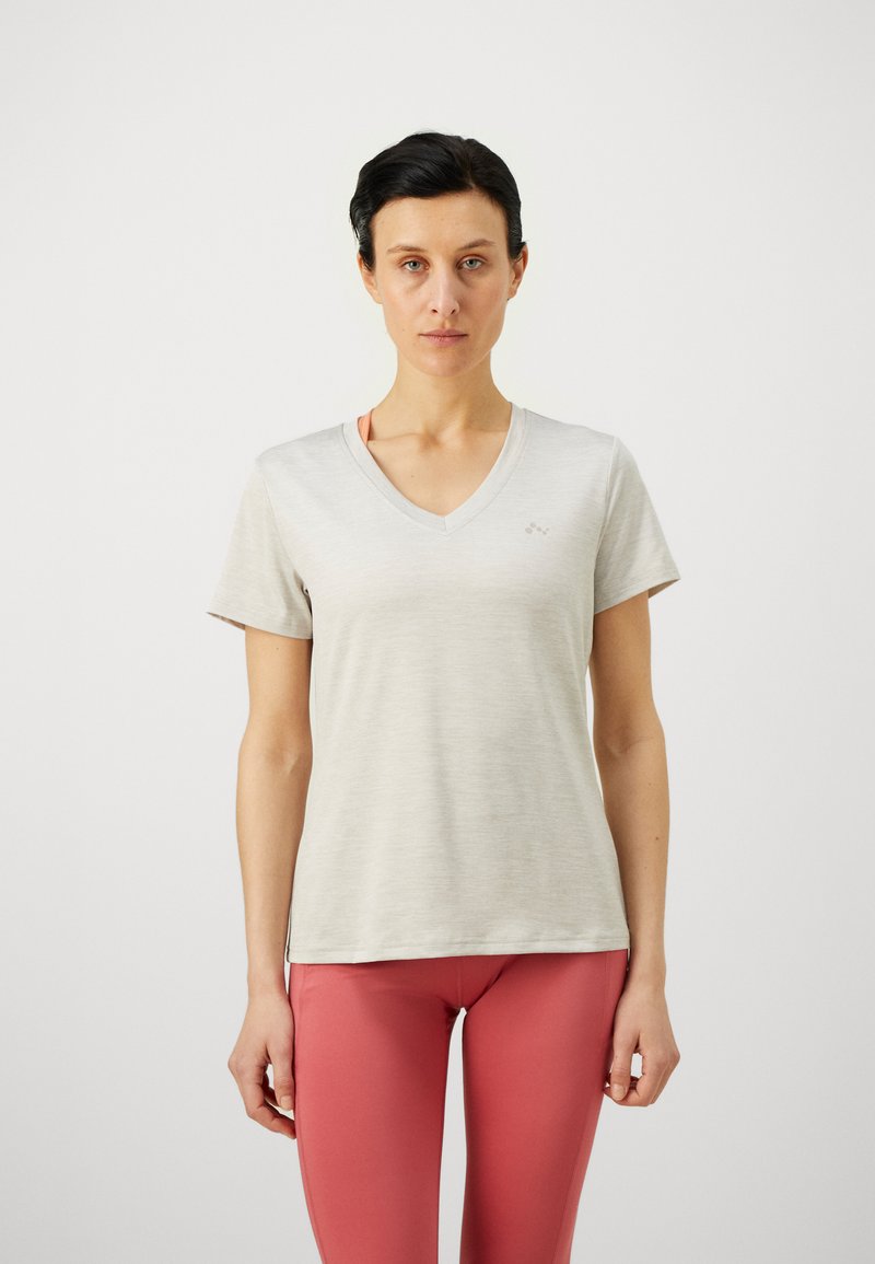 Lys grå V-hals T-shirt i et blødt stof, kortærmet, med et subtilt logo på brystet. Sammen med koralfarvede leggings.