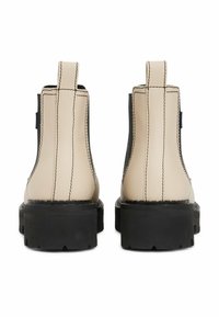 Stivaletti in pelle beige con suole in gomma nere, caratterizzati da cuciture evidenti e linguette laterali per indossarli facilmente.