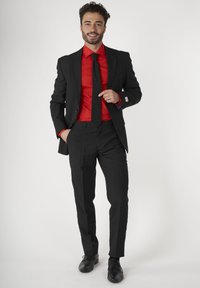 Zwart pak met een slim-fit ontwerp, gecombineerd met een gestructureerd rood overhemd en een zwarte stropdas. Zwarte dresschoenen maken de look compleet.
