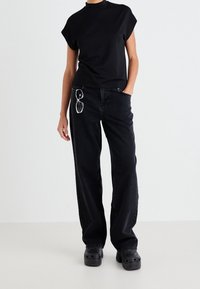 Svart t-shirt med kapuppar, tillsammans med vida svarta jeans. Tillbehör inkluderar solglasögon på kedja. Svarta träskor fulländar outfiten.