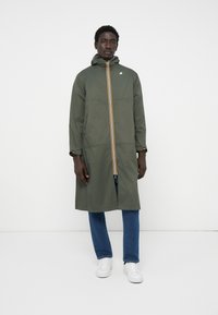 Impermeabile verde oliva con cappuccio, dotato di zip centrale e strisce giallo-arancio. Taglio slim con maniche lunghe e chiusure ai polsi.
