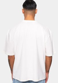 Hvid bomulds t-shirt med en løs pasform, dropped shoulder seams og rund halsudskæring, vist fra bagsiden.
