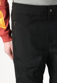 Pantalon cargo noir en tissu texturé, doté d'une poche zippée sur le côté et d'une taille légèrement élastique pour un ajustement sécurisé.