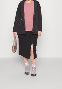 Svart zip-jacka över en rosa topp, kombinerat med en svart ribbad kjol med en sidoflik. Grå sneakers och en mönstrad handväska fulländar looken.