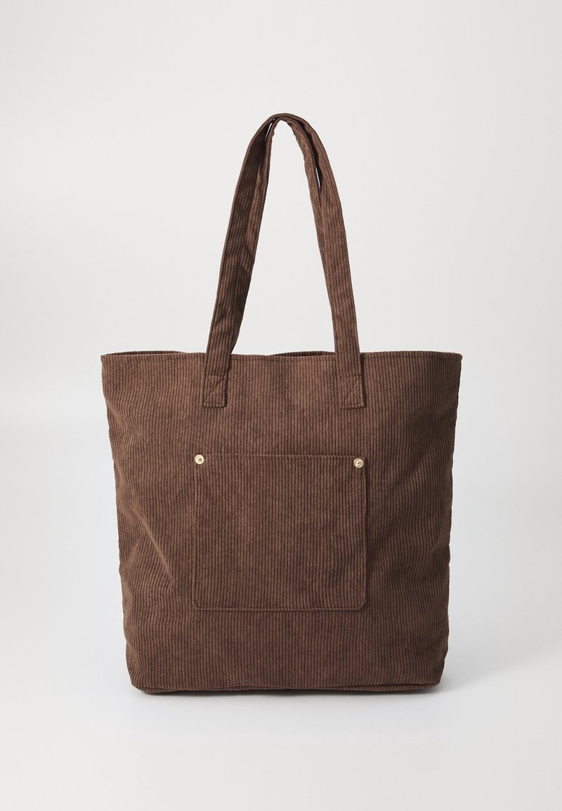 Sac cabas en velours côtelé marron avec longues anses et poche avant sécurisée par deux petits rivets métalliques.