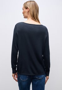 Dunkelblauer Pullover mit langen Ärmeln, weitem Ausschnitt, glatter Textur und lässigem Schnitt, kombiniert mit blauen Jeans.