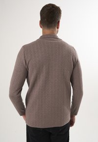 Bruine gebreide trui met een gestructureerd zigzagpatroon, met een kraag-halslijn en lange mouwen. Achteraan is de ontspannen pasvorm en zoom zichtbaar.