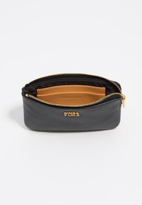 Zwarte leren pouch met een gestructureerde afwerking, gouden rits en gouden logo. Het interieur heeft een tan kaartvak tegen een zwarte voering.