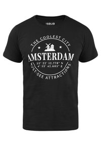 Sort bomulds T-shirt med hvidt print, der viser "Amsterdam," koordinater og illustrationer af en vindmølle og bygninger. Rund hals design.