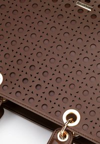 Borsa a tracolla marrone con perforazioni, caratterizzata da tagli circolari e triangolari, accessori in tono oro e una superficie in pelle liscia.