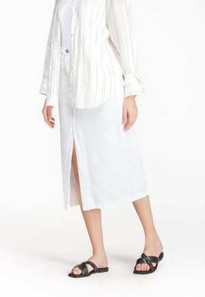 Witte midi-jurk met een zijsplit, gemaakt van een soepele stof. Gepaard met zwarte slide-sandalen en een licht gestreepte overhemd met knopen.