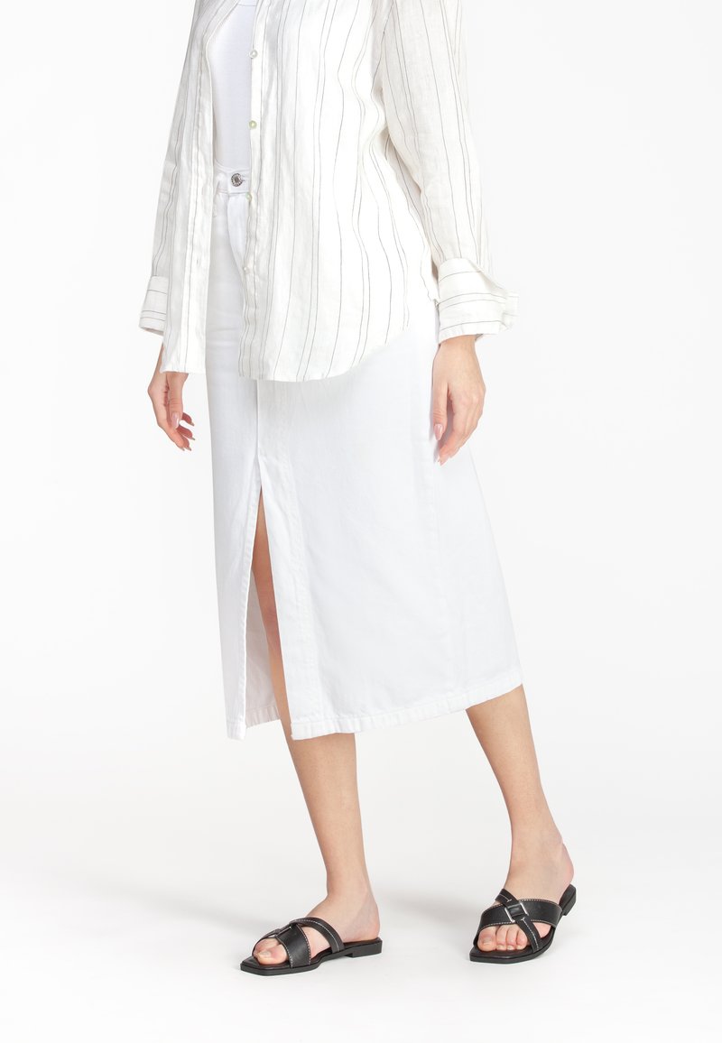 Hvid midi-nederdel med sideslids, lavet af glat stof. Kombineret med sorte slidesandaler og en lys stribet button-up skjorte.