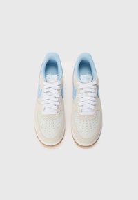 Light beige sneakers with suede uppers, blue accents, and white laces. Features perforated toe and gum sole. Nike branding on tongue.