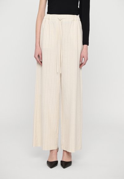 Pantaloni beige a gamba larga con righe verticali, vita elastica e dettaglio con cordoncino, abbinati a tacchi neri a punta.
